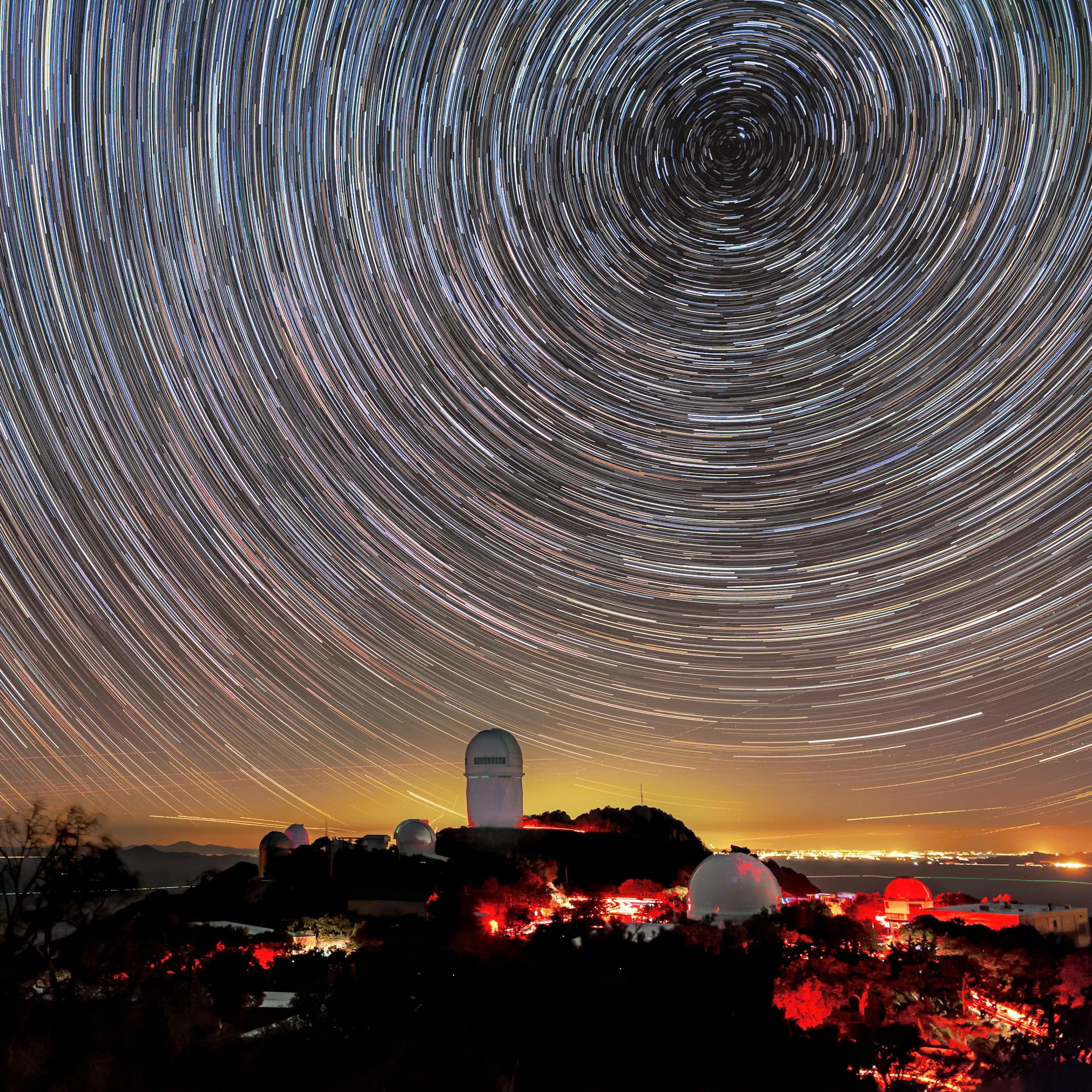 Timelapse photo showing star trails in the night sky above a large telescope building.