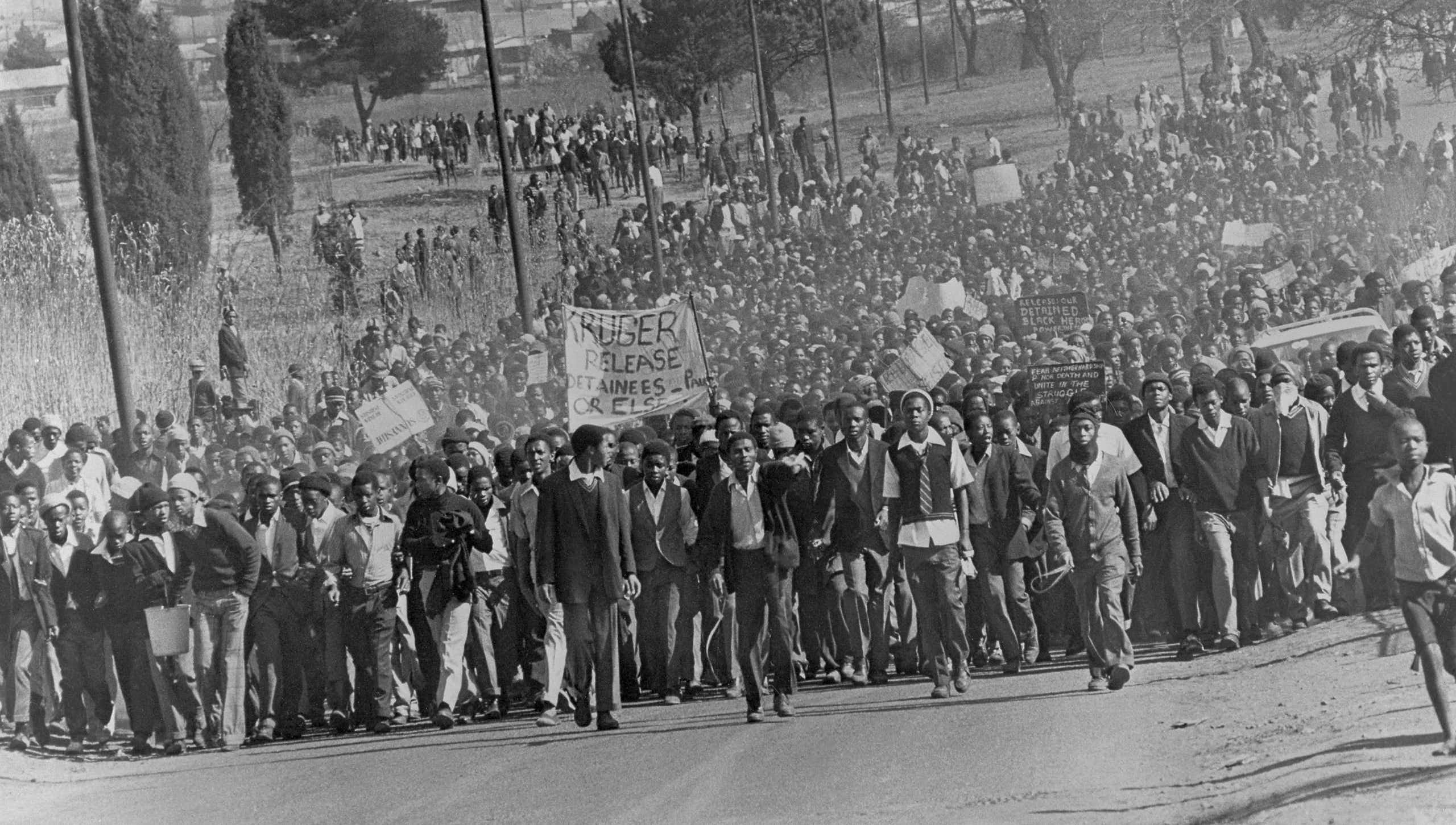 A sea of young Africans, some win school uniforms, marches down a road, placards, banners and fists aloft.