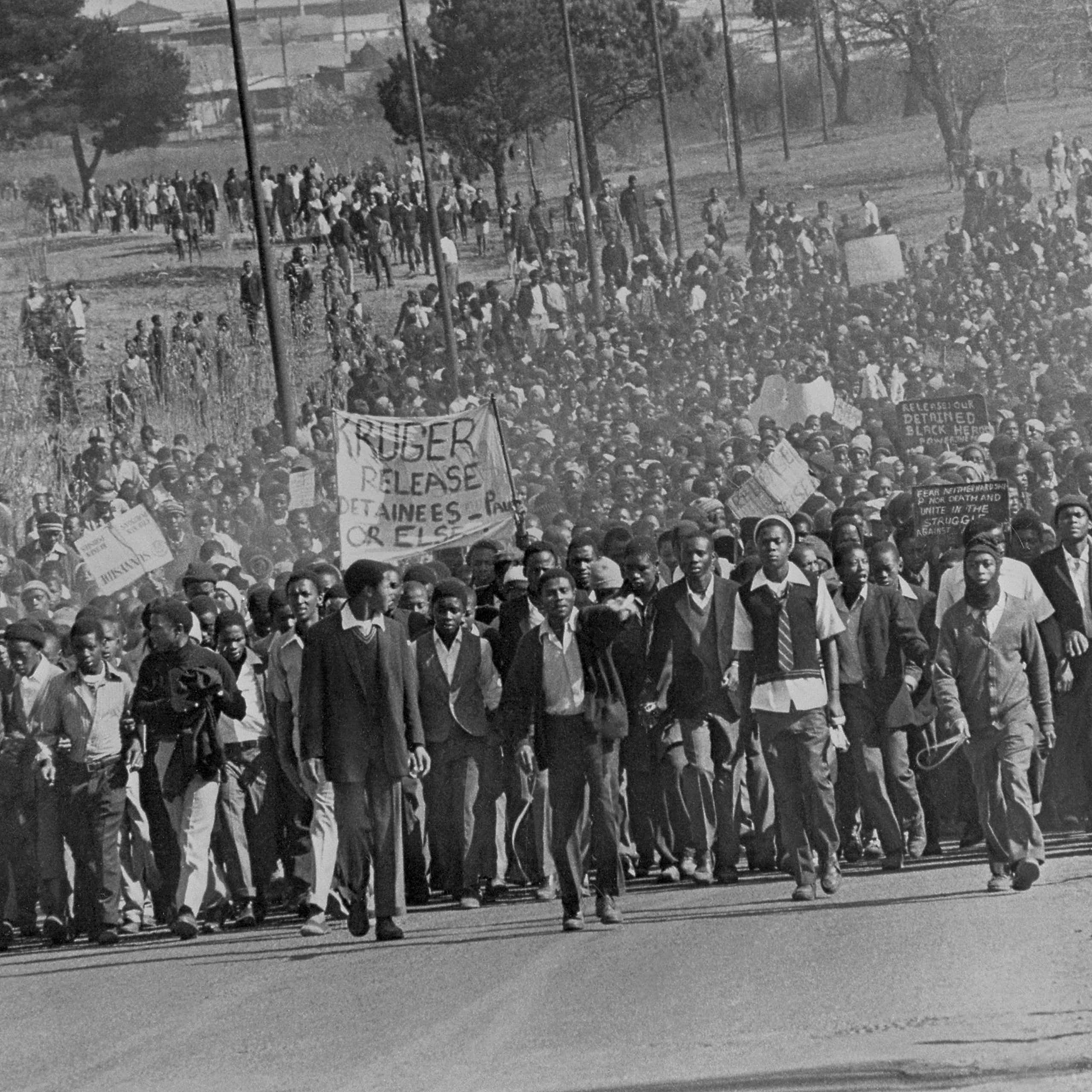 A sea of young Africans, some win school uniforms, marches down a road, placards, banners and fists aloft.