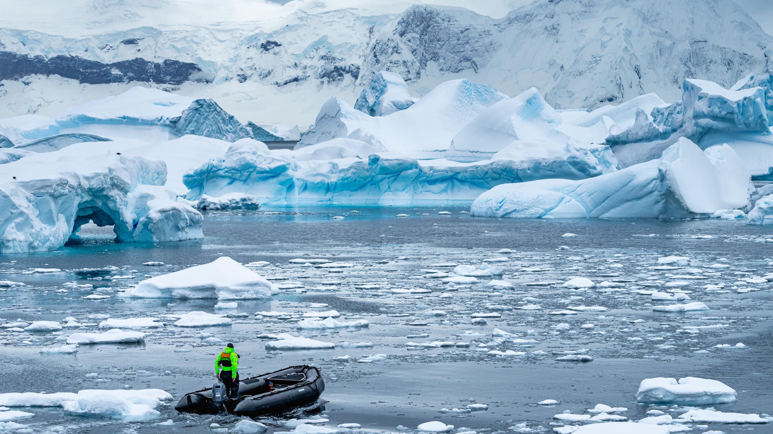 A small boat drives through melted ice with a backdrop of ice bergs and shelves.