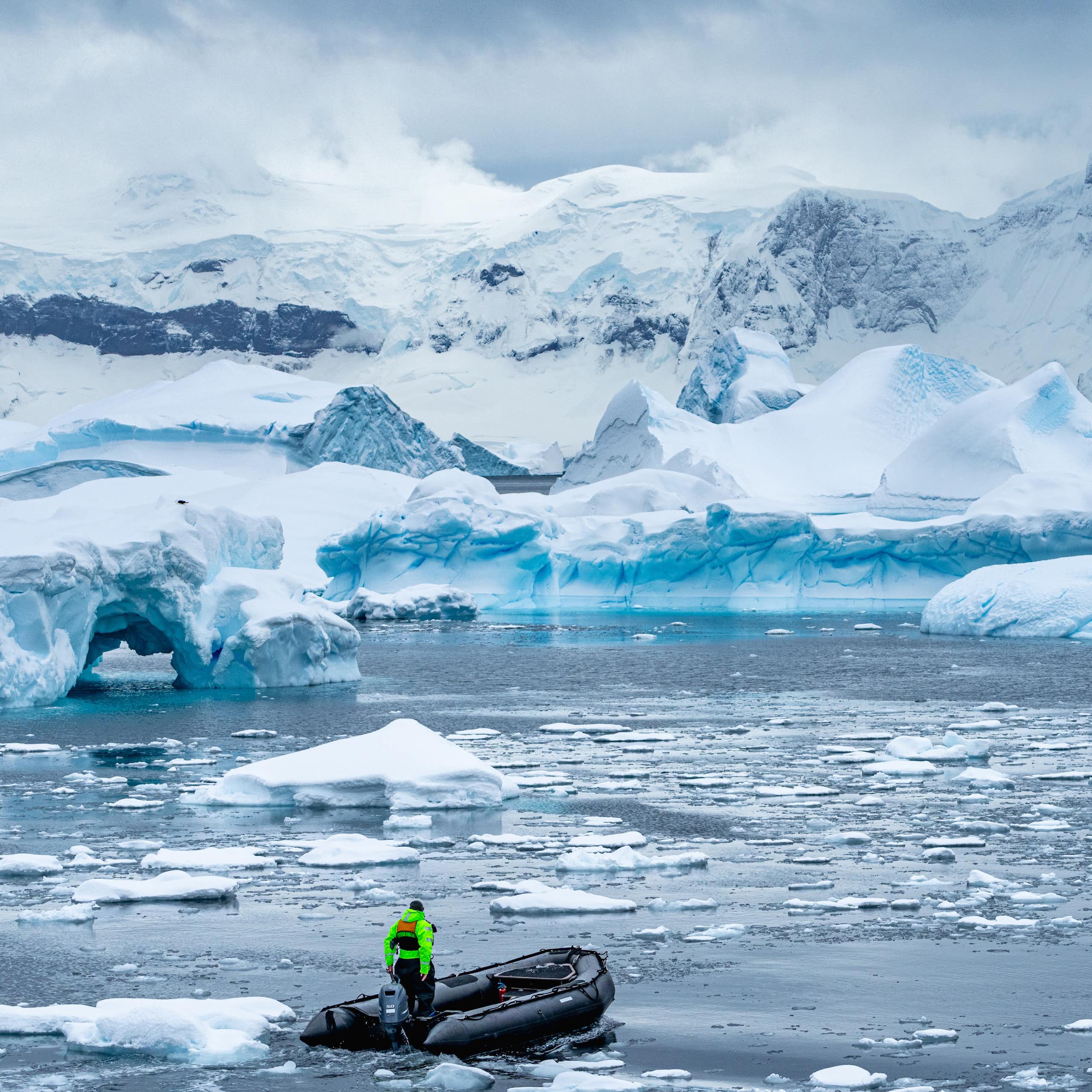 A small boat drives through melted ice with a backdrop of ice bergs and shelves.