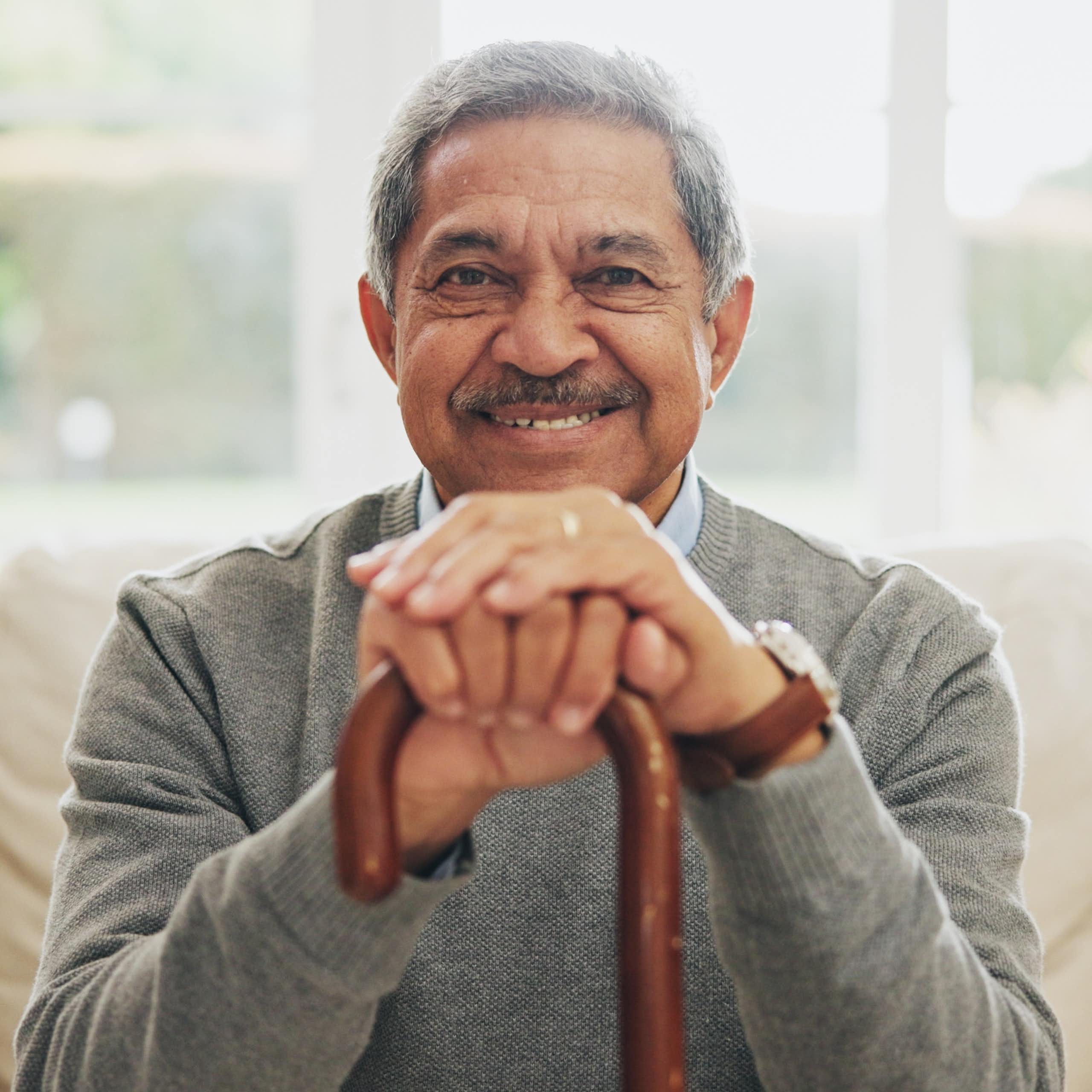 A man with gray hair and a mustache smiling and holding a cane