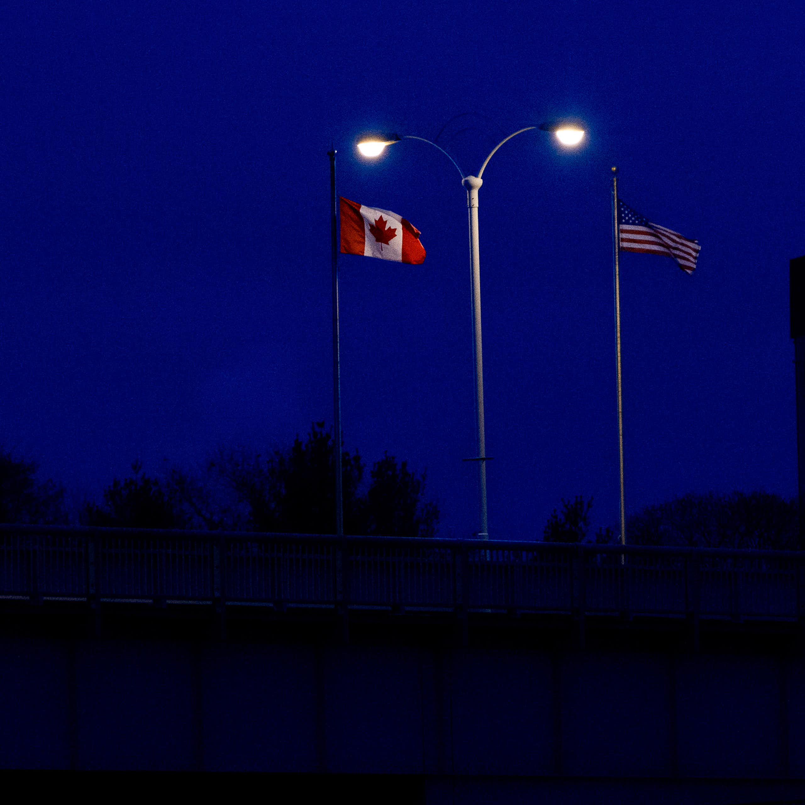 Flag with maple leaf and flag with stars and stripes spotlit by lights at night.
