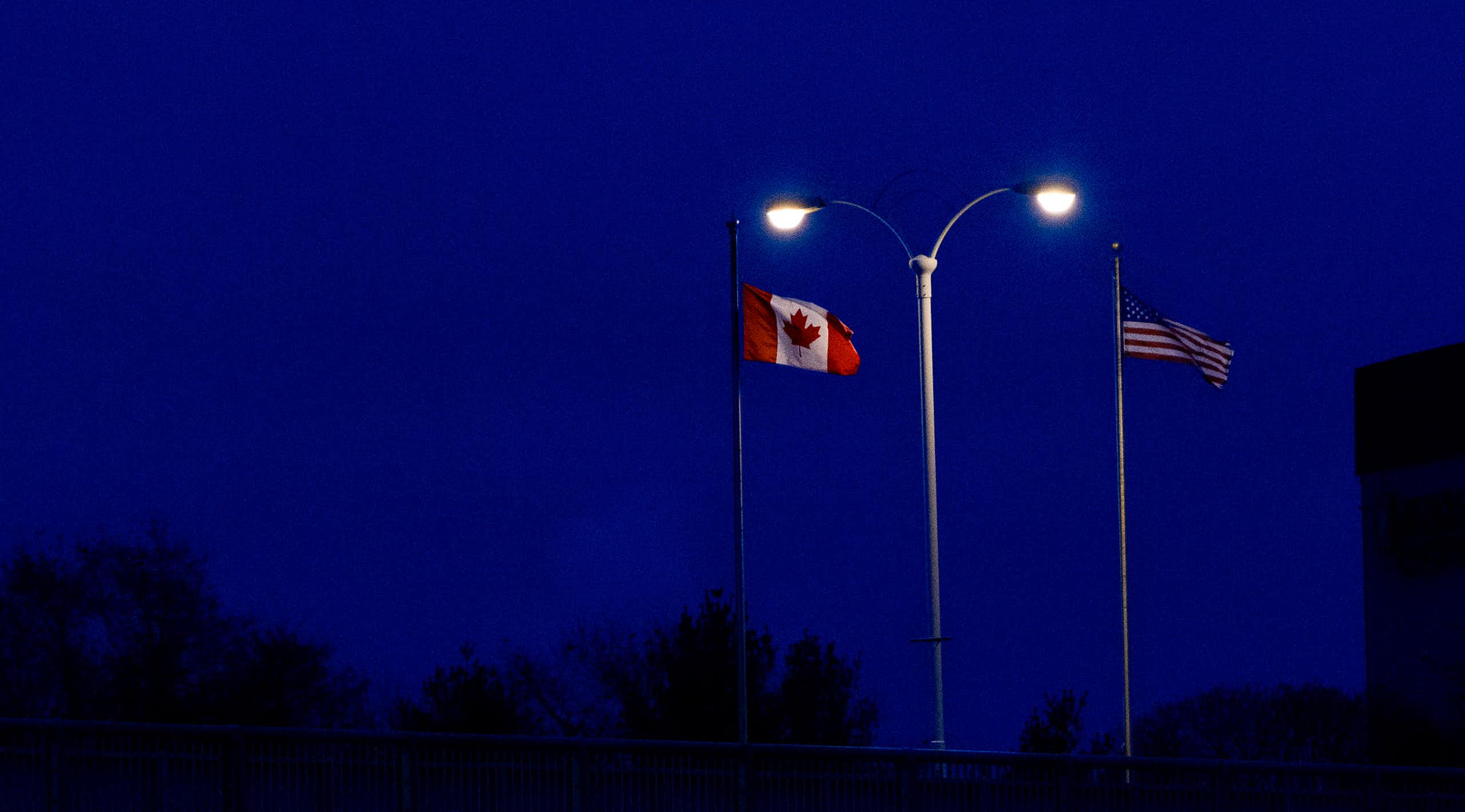 Flag with maple leaf and flag with stars and stripes spotlit by lights at night.