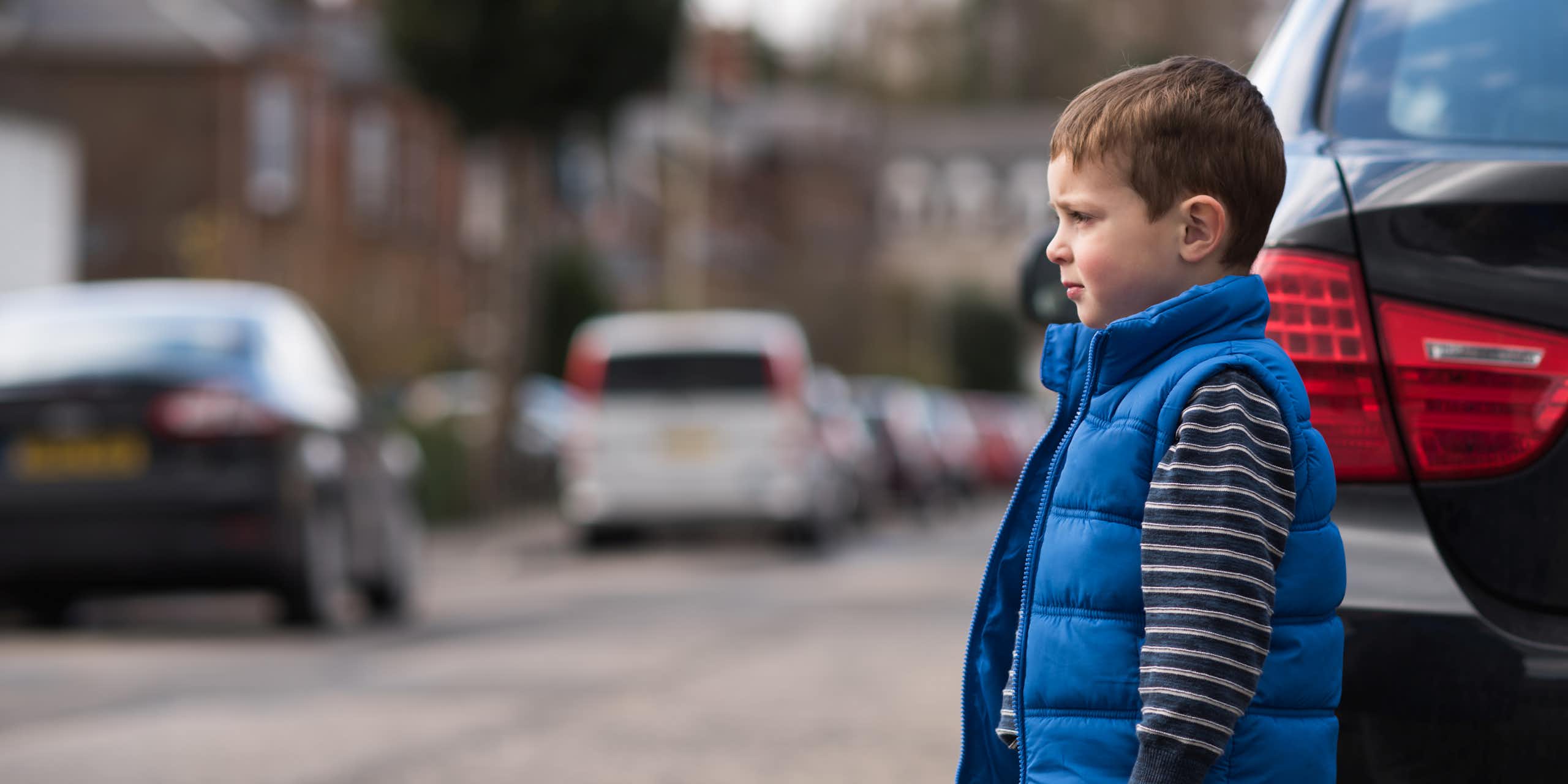 A boy crossing the street between parked cars.