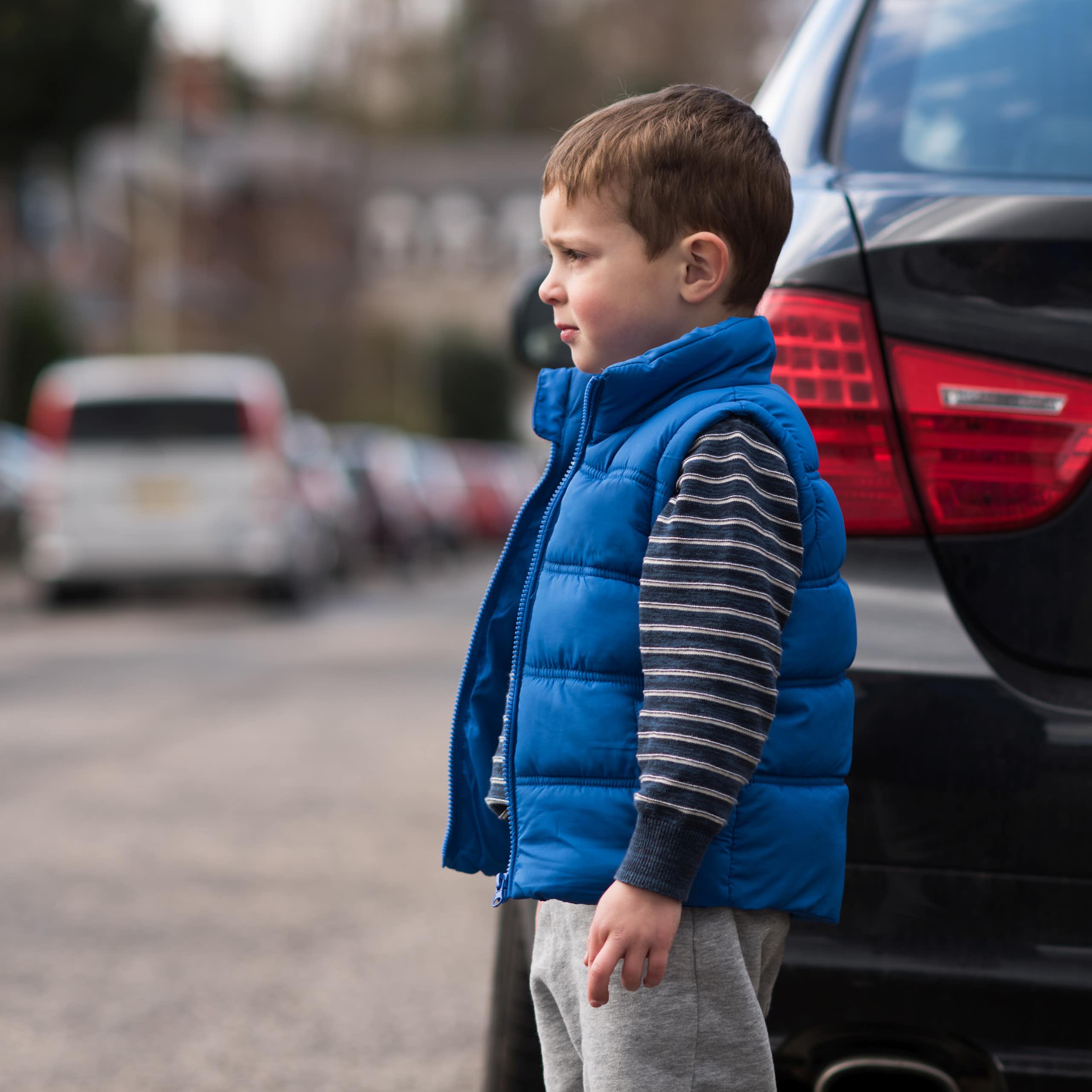 A boy crossing the street between parked cars.