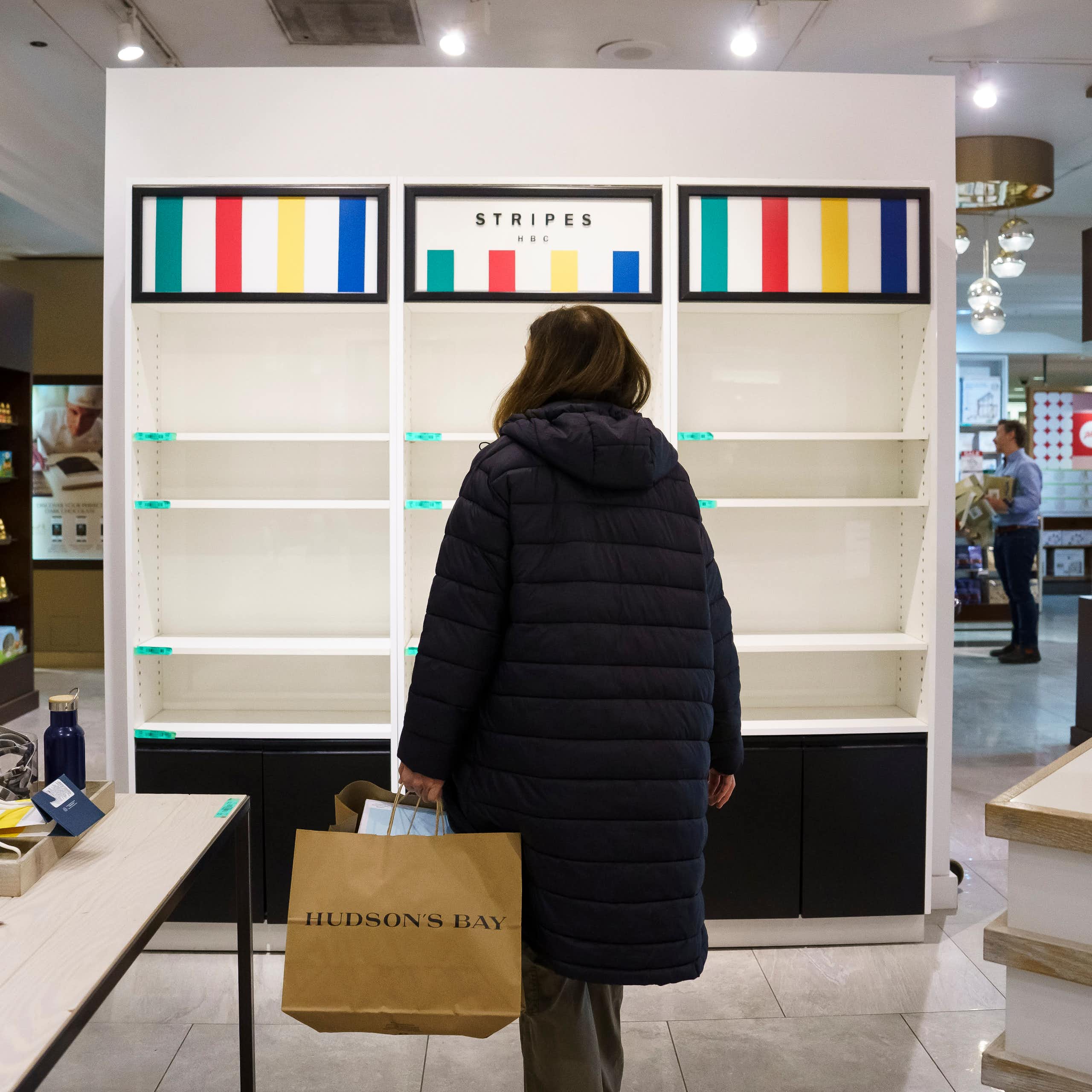 A woman, seen from behind, stands in front of empty shelves in a department store