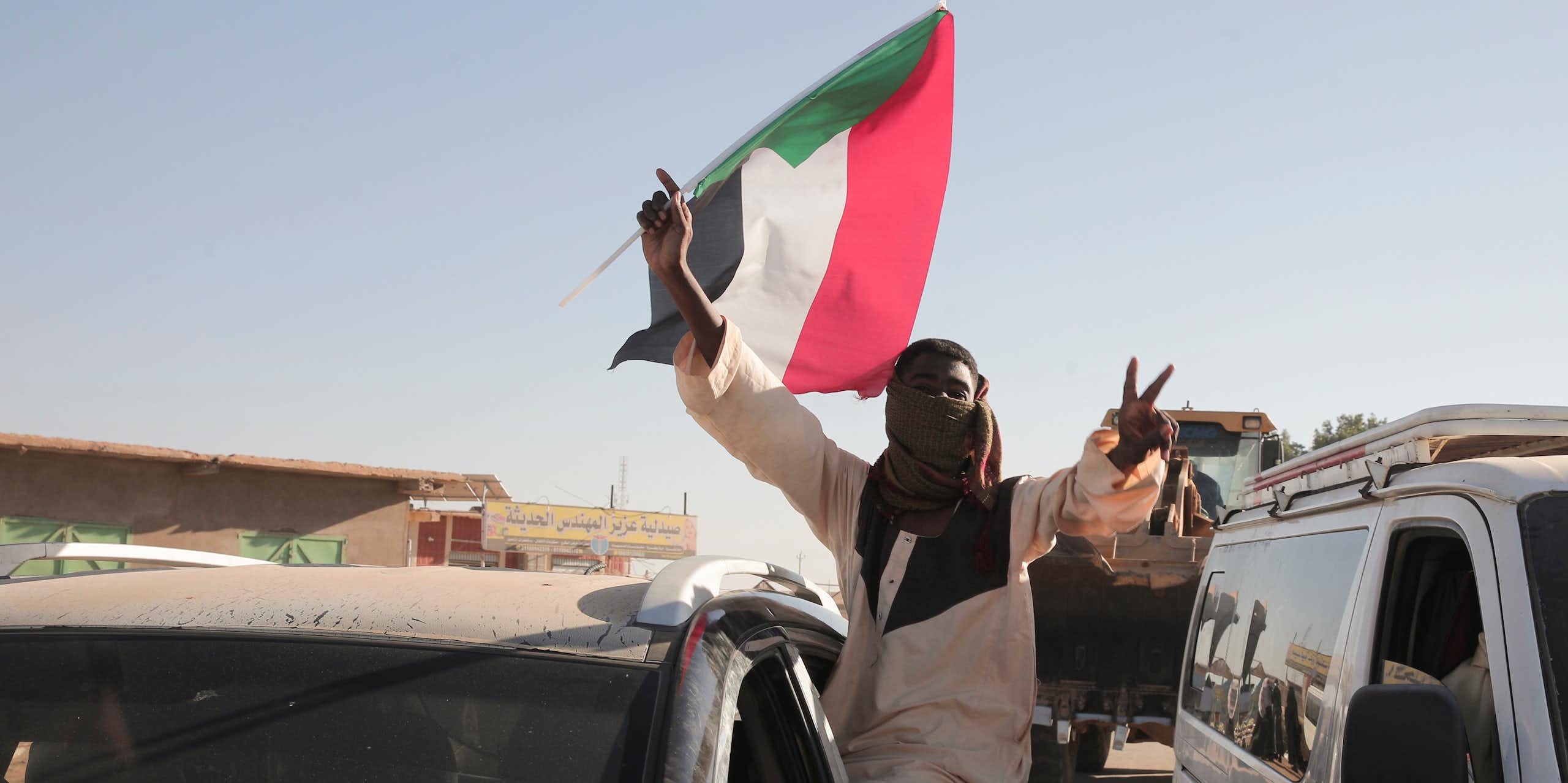 A man flashes victory V signs while holding a red, white, black and green flag.