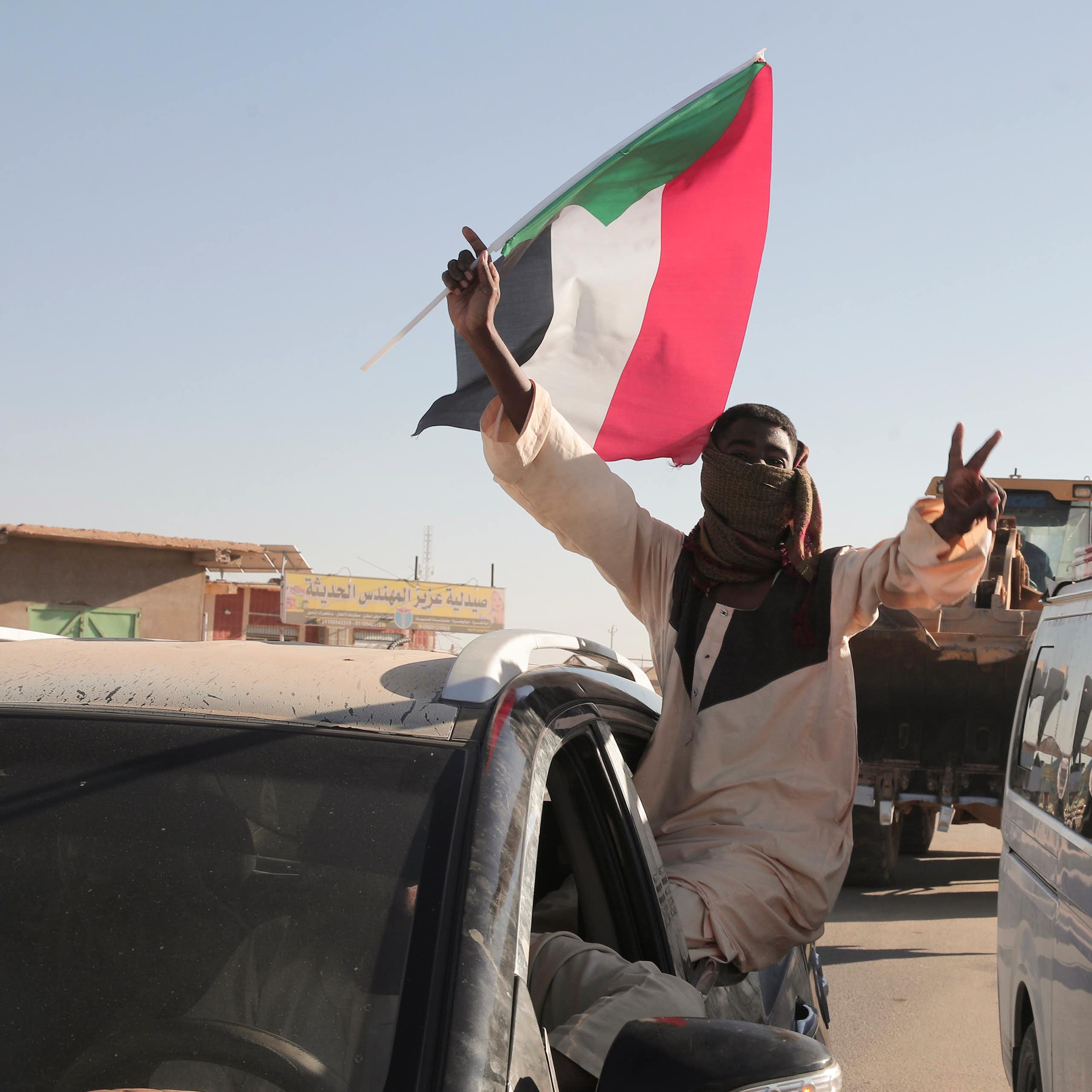 A man flashes victory V signs while holding a red, white, black and green flag.