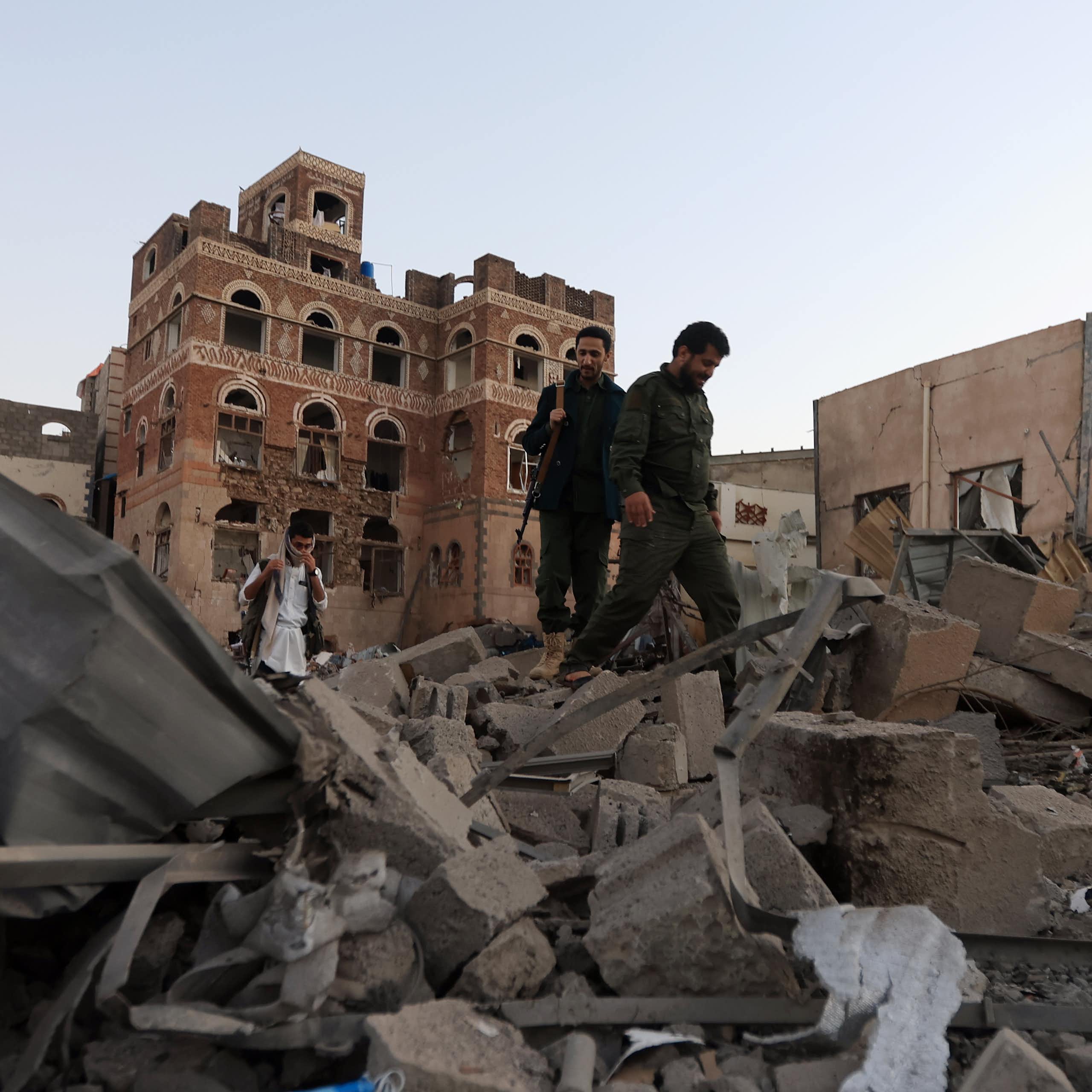 People holding guns walk through piles of rubble.
