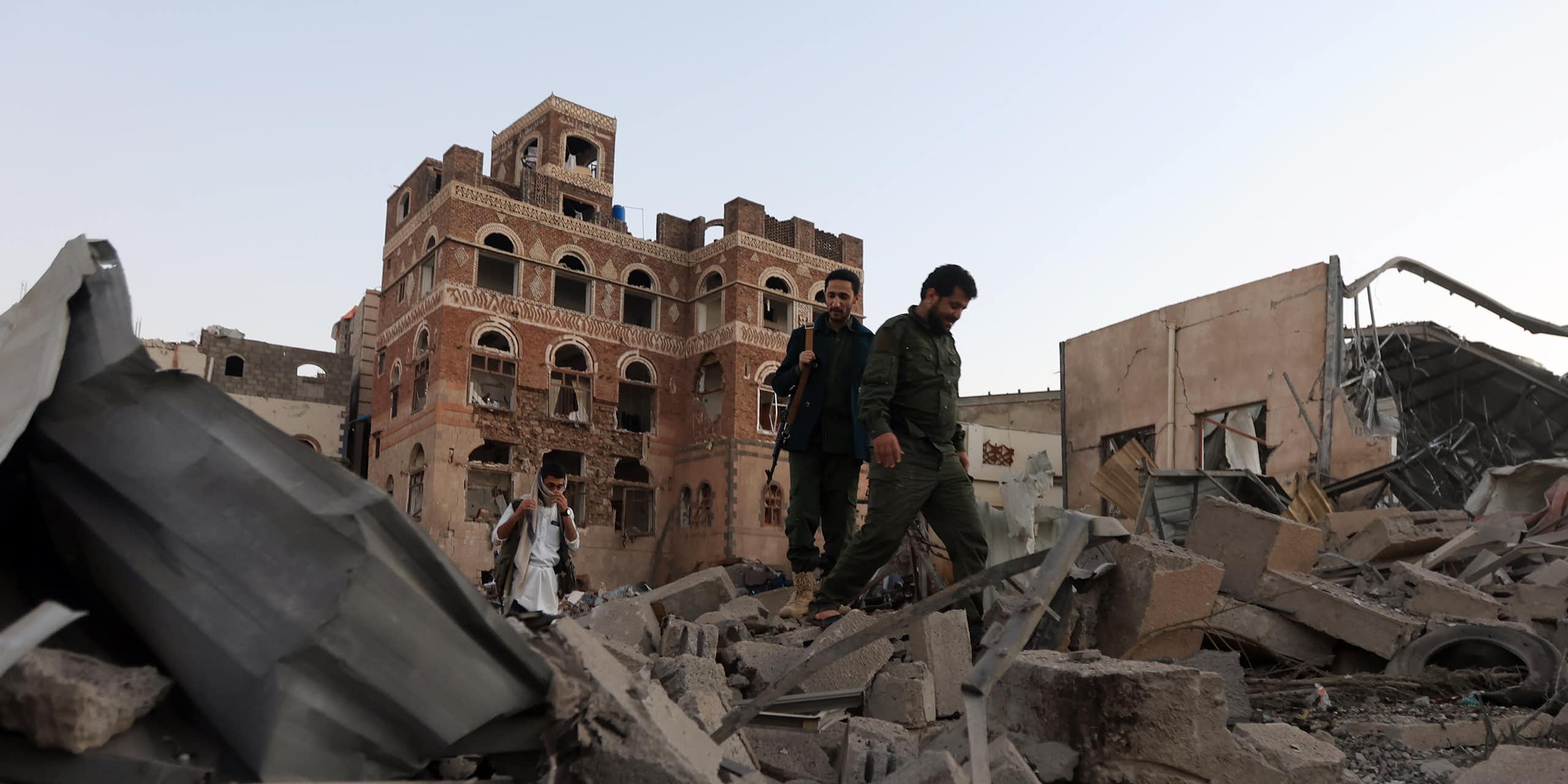 People holding guns walk through piles of rubble.