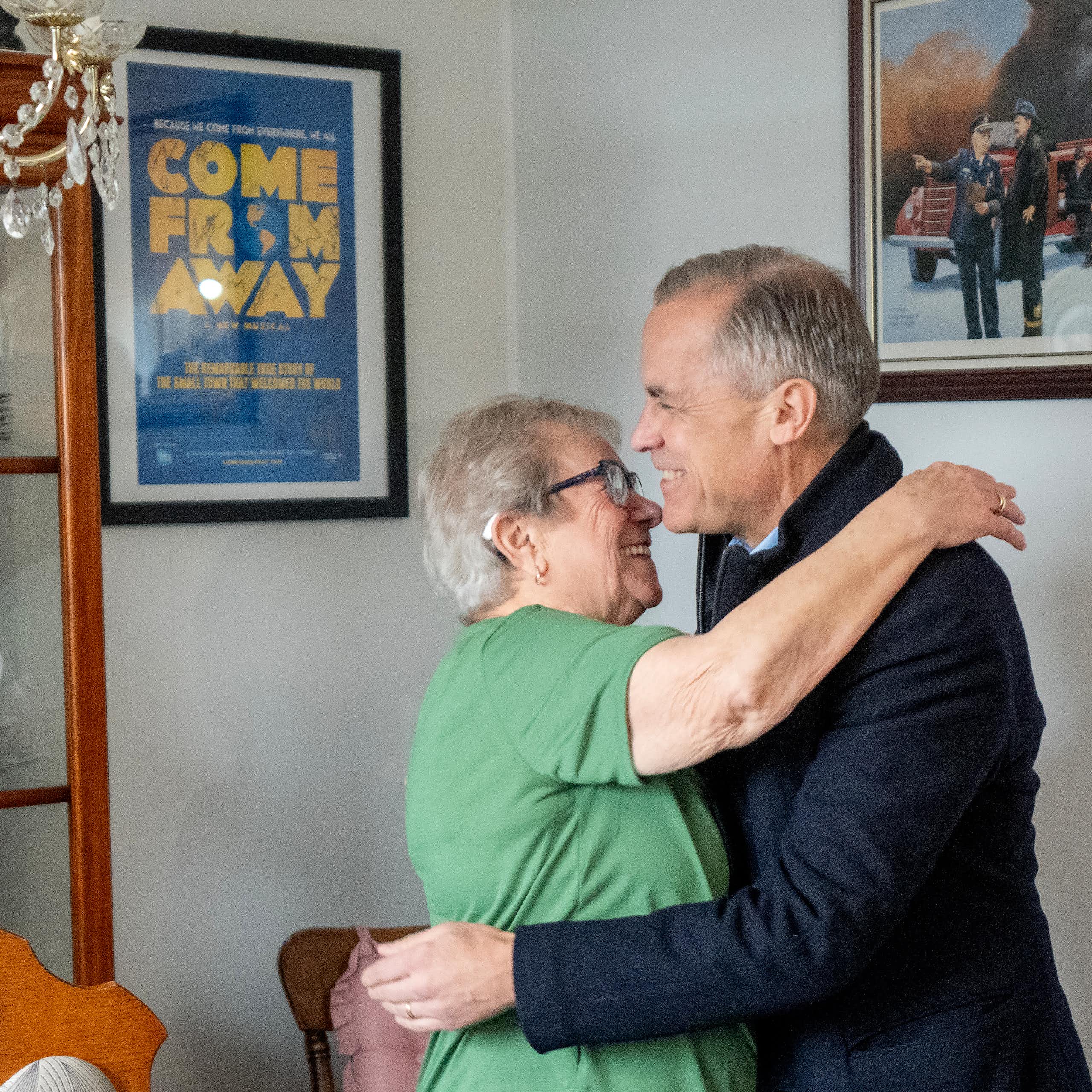 An older woman in a green shirt hugs a man with short grey hair.
