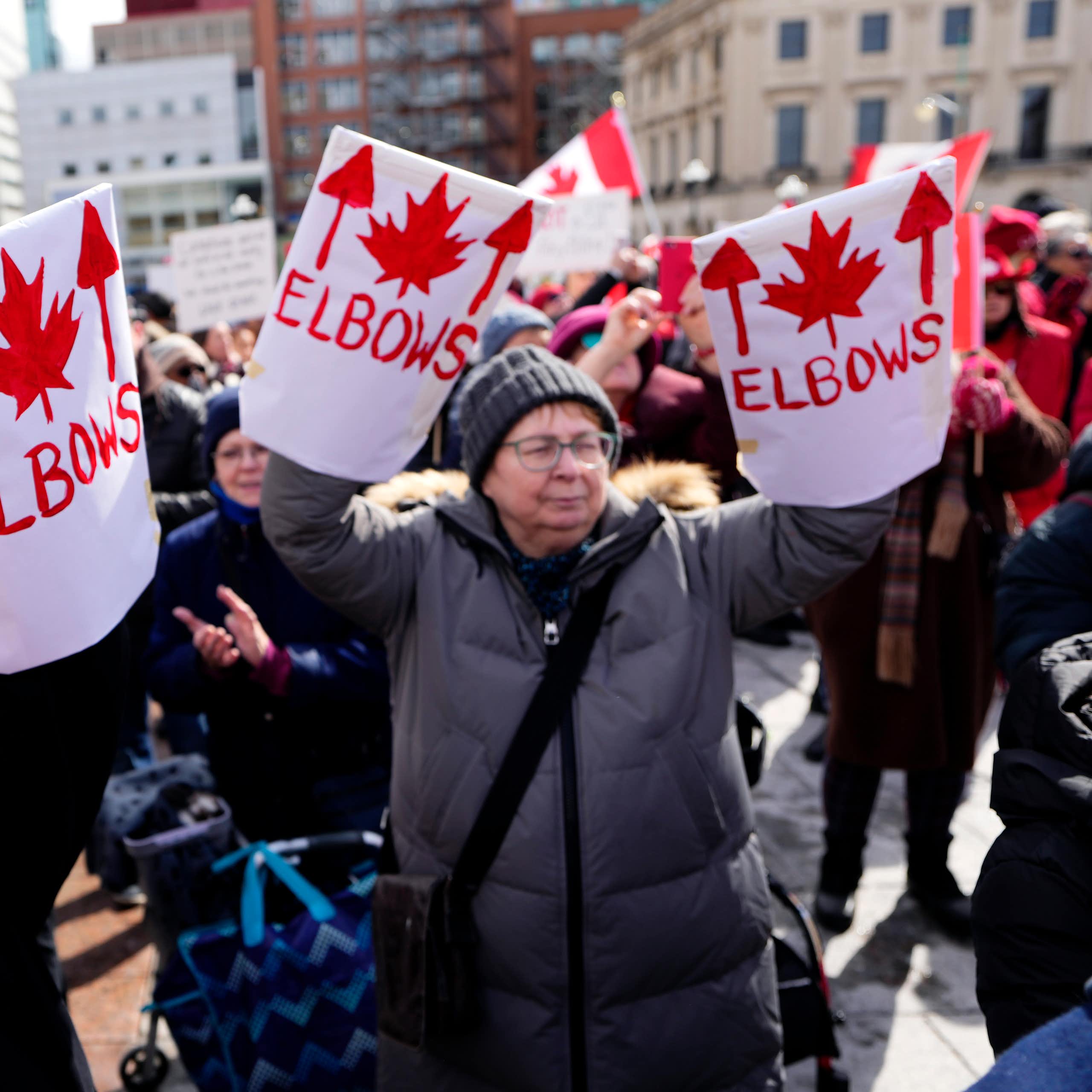 Middle-aged women hold up Elbows Up signs at a protest.