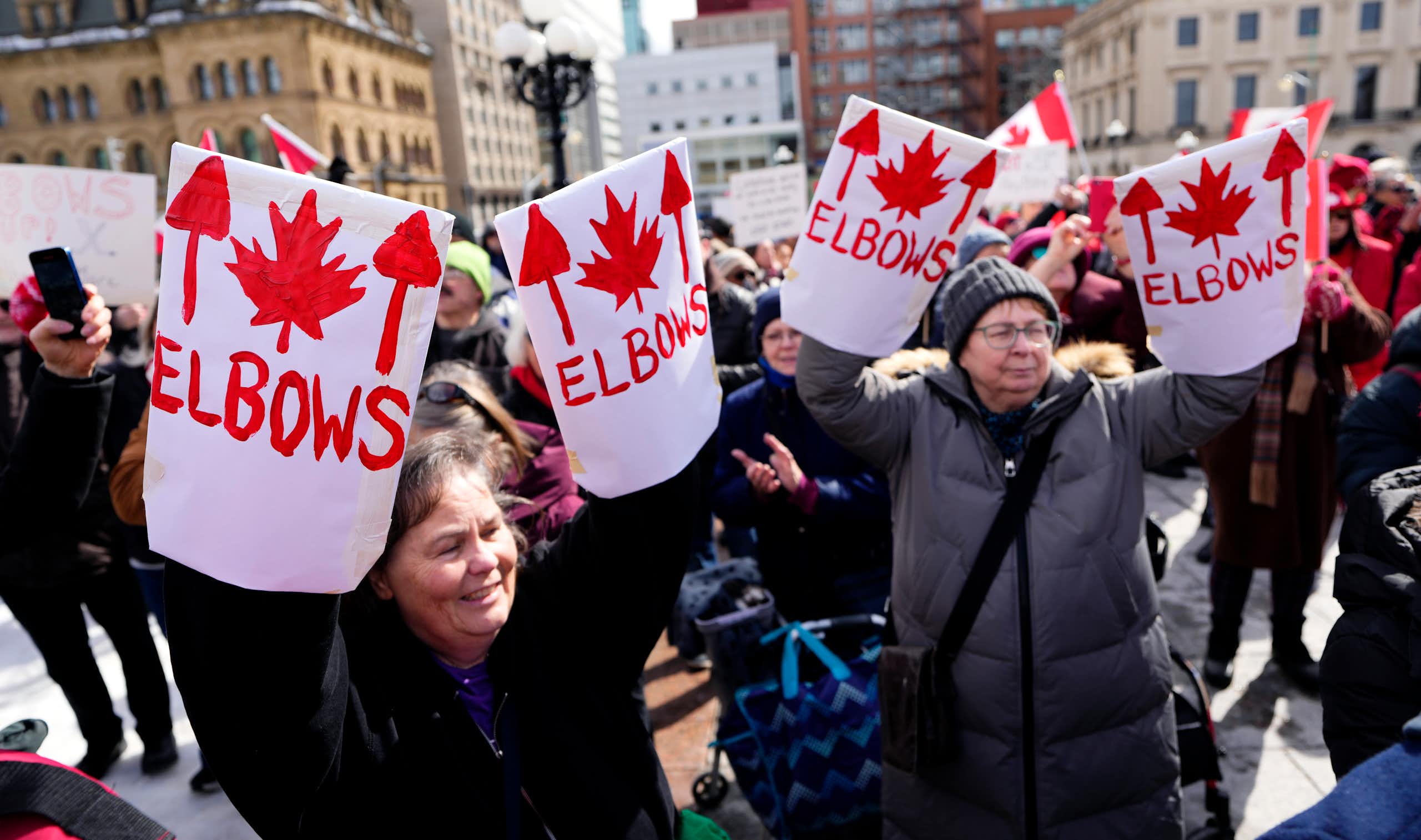 Middle-aged women hold up Elbows Up signs at a protest.