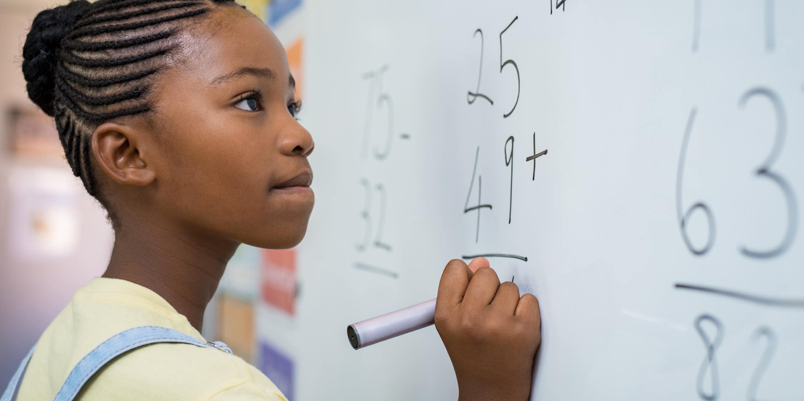 Schoolgirl solving addition sum on white board with marker pen. 