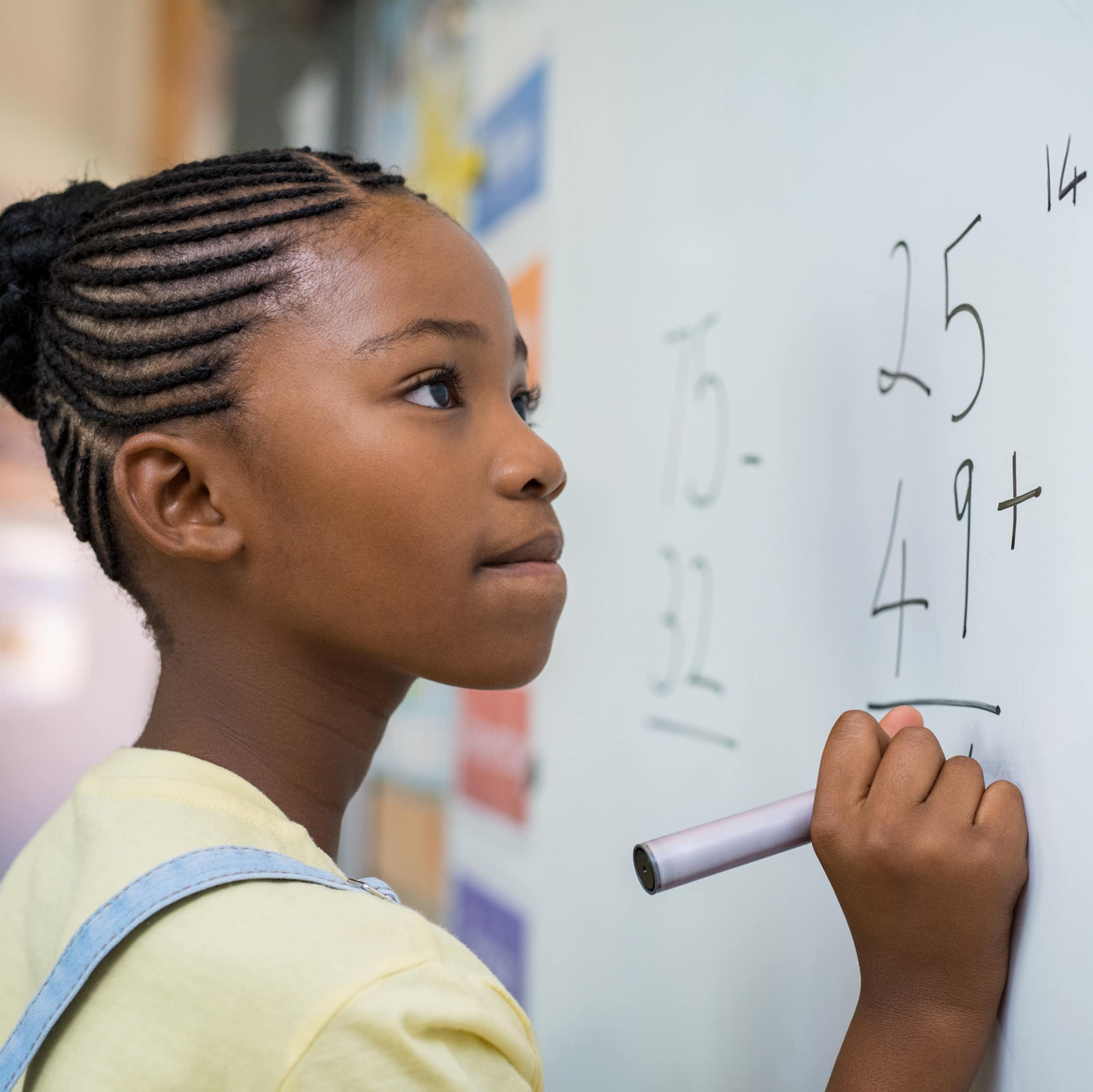 Schoolgirl solving addition sum on white board with marker pen. 