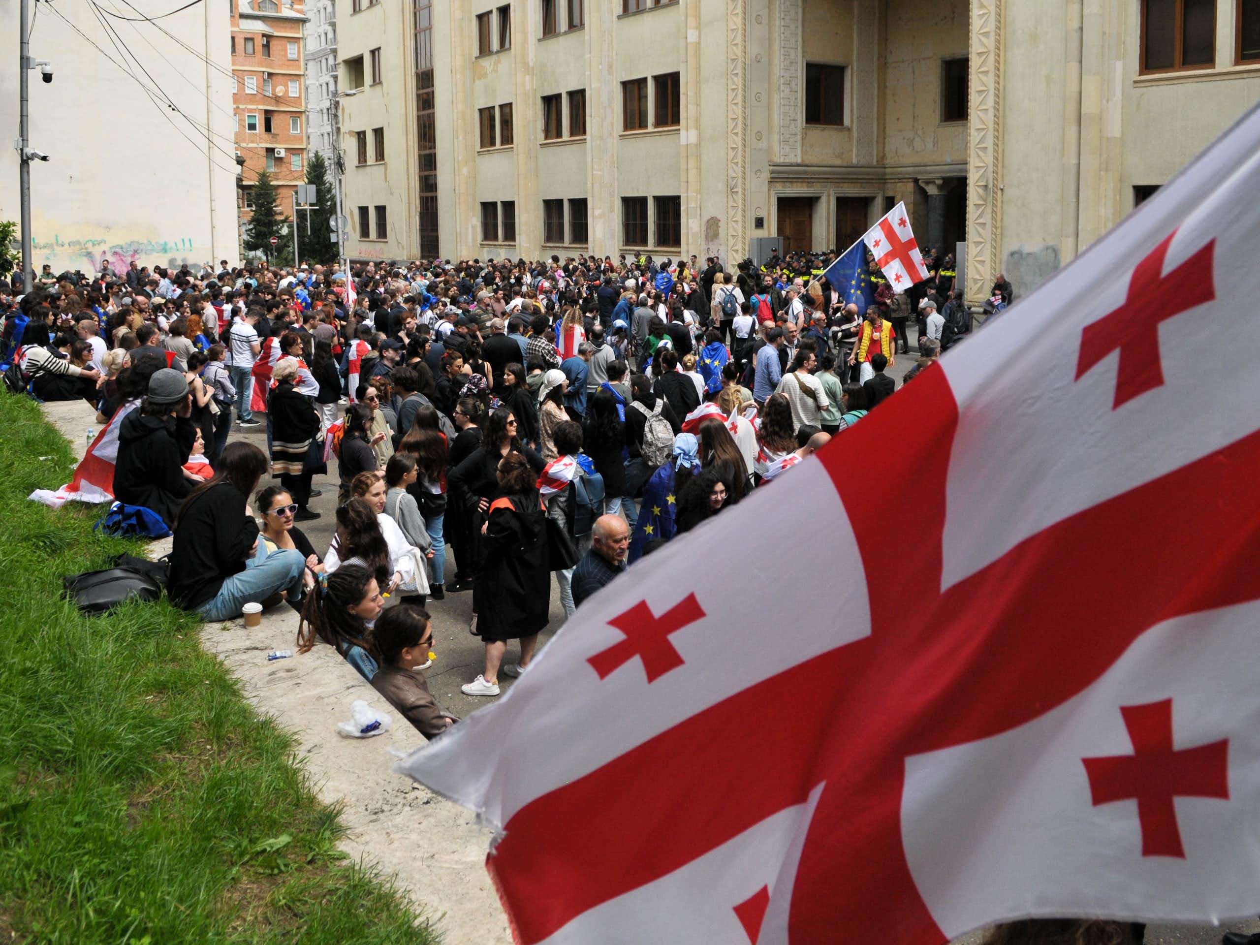 A large red and white flag is seen in front of a crowd of people.