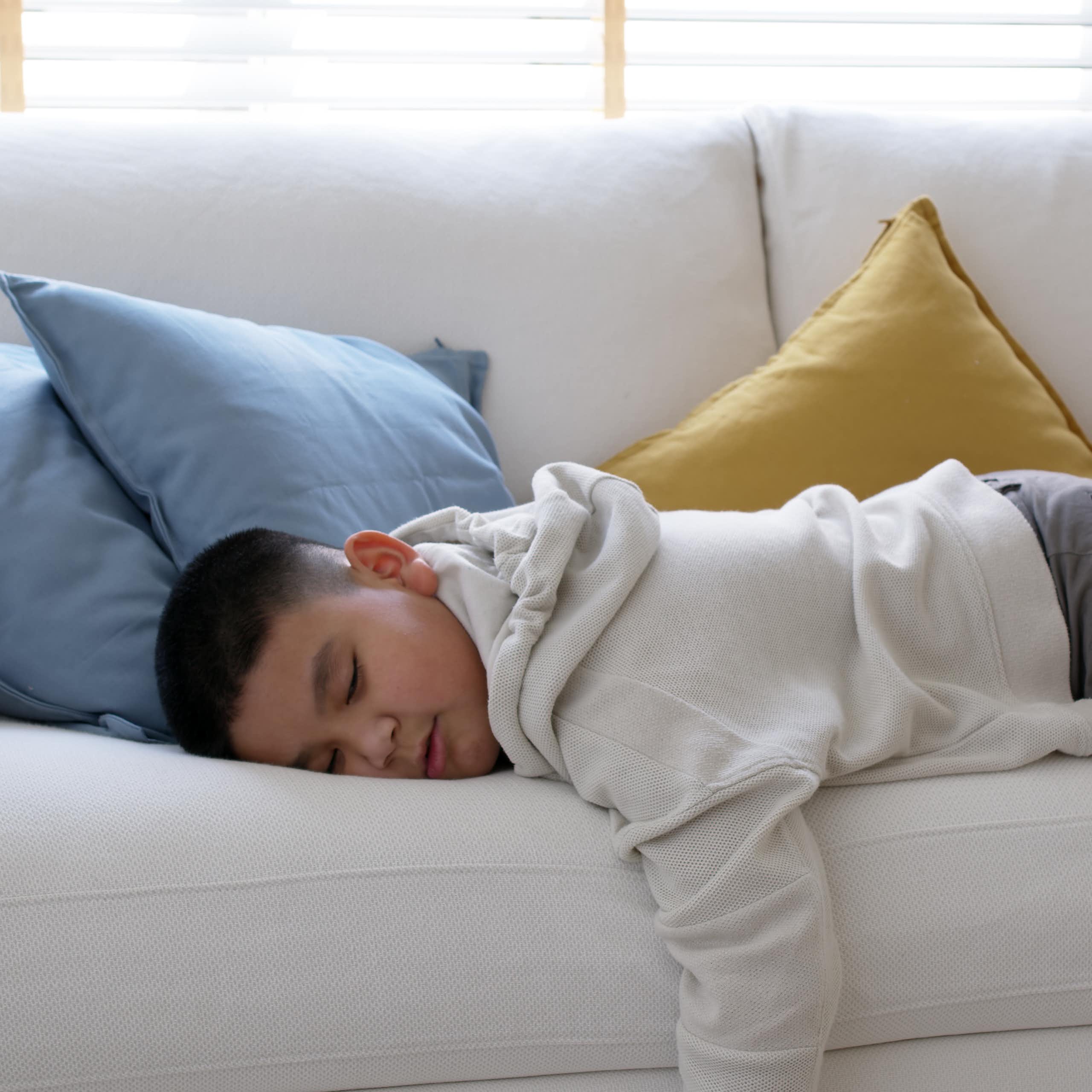 A young boy lies on the couch asleep. 