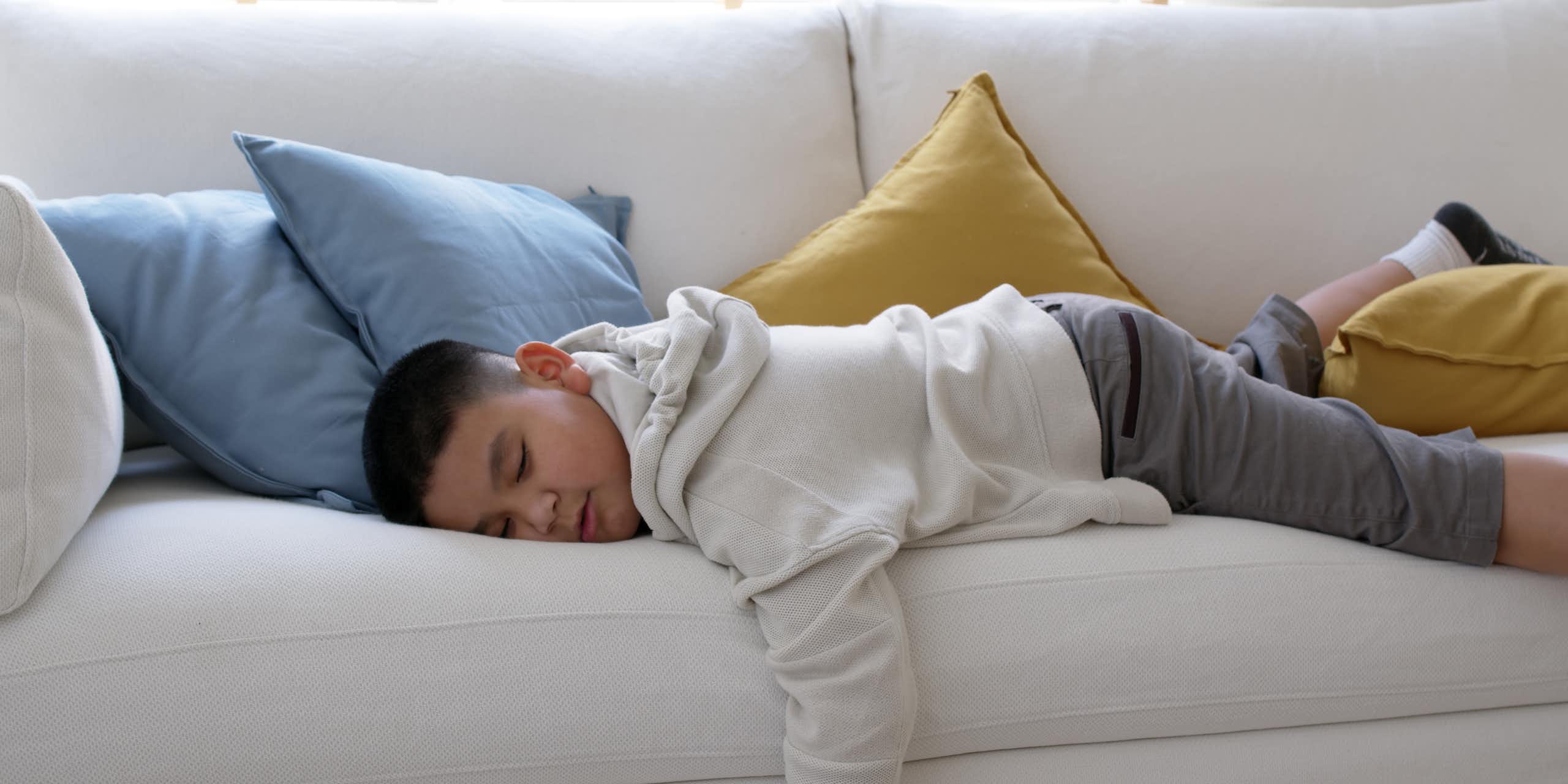 A young boy lies on the couch asleep. 