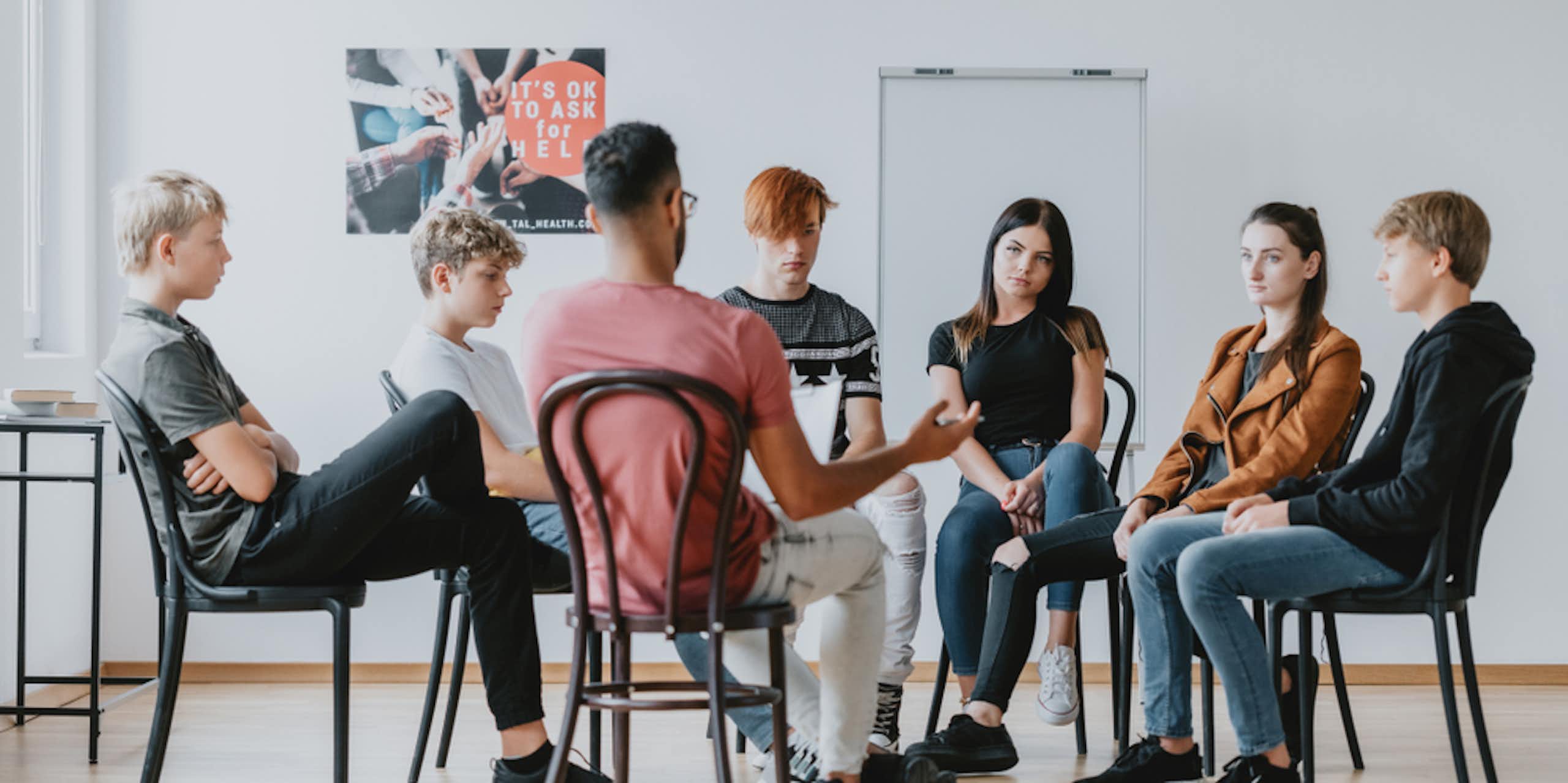 Group of teenagers sitting on chairs in a circle with a therapist or teacher leading discussion